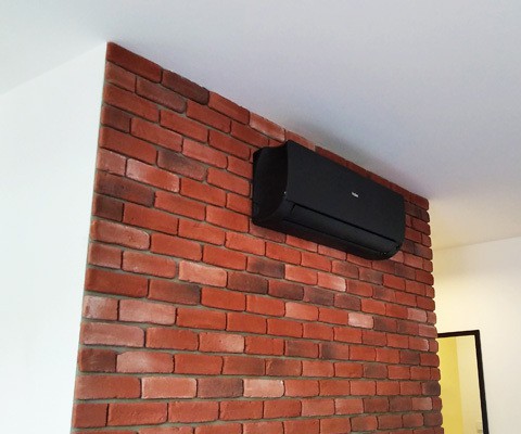 Czarna jednostka wewnętrzna Haier zamontowana na ceglanej ścianie w mieszkaniu w Krakowie