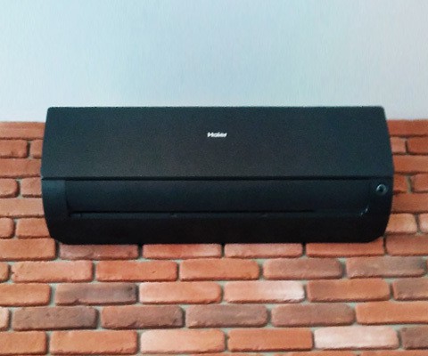 Zbliżenie na czarną jednostkę wewnętrzną Haier zamontowaną na ceglanej ścianie w Krakowie